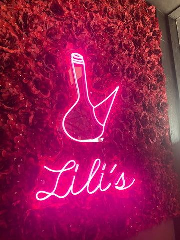 Custom neon sign with a bright pink beer mug icon and the word Lili on a red flower wall