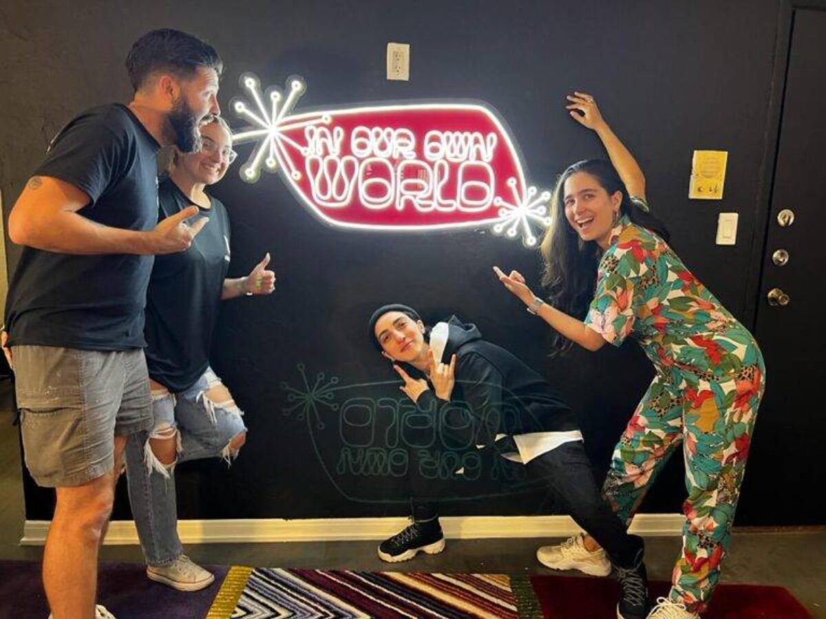 People posing in front of a custom neon sign with red and white light tubing on a dark wall