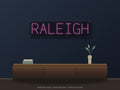Raleigh City Name Neon Sign shown above a walnut console in a styled room mockup